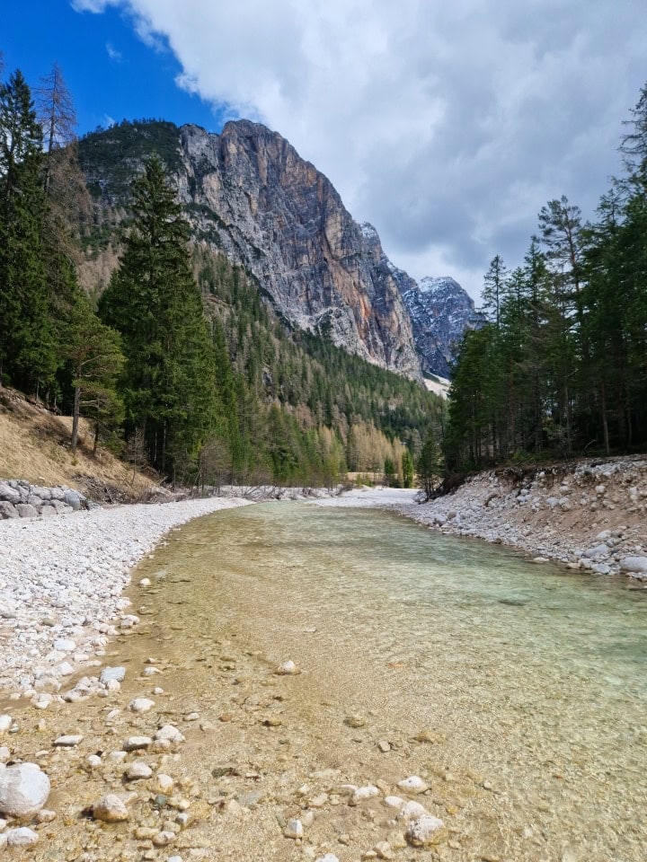 a turquoise river boite with huge mountains in the background - there's still snow on some of them in april in dolomites italy