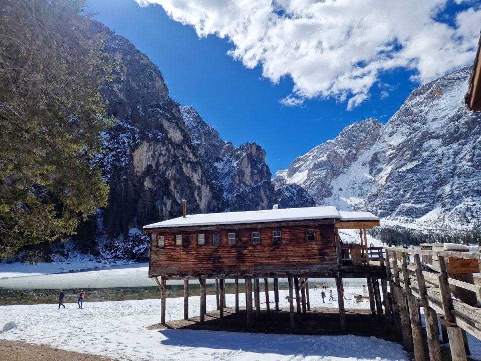 boat house by lago braies with mountains, blue sky, green waters, and a lot of snow in dolomites in april italy