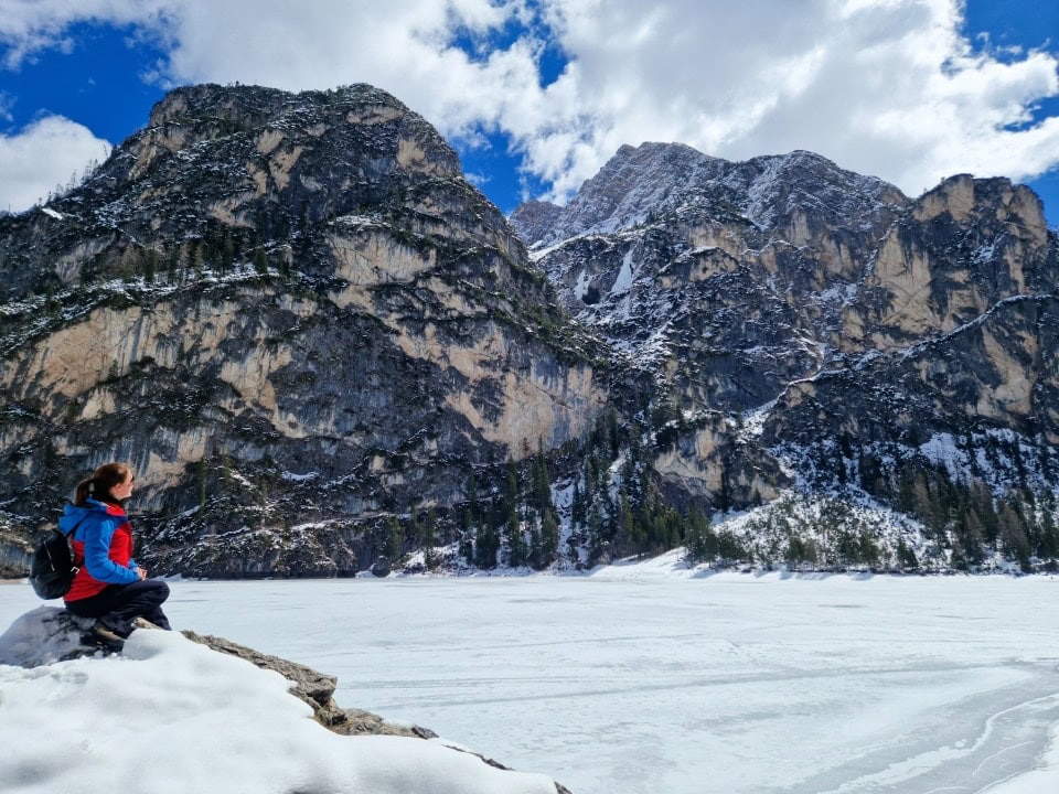 enjoying the views around the snowy lake braies in dolomites in italy while sitting on a huge rock