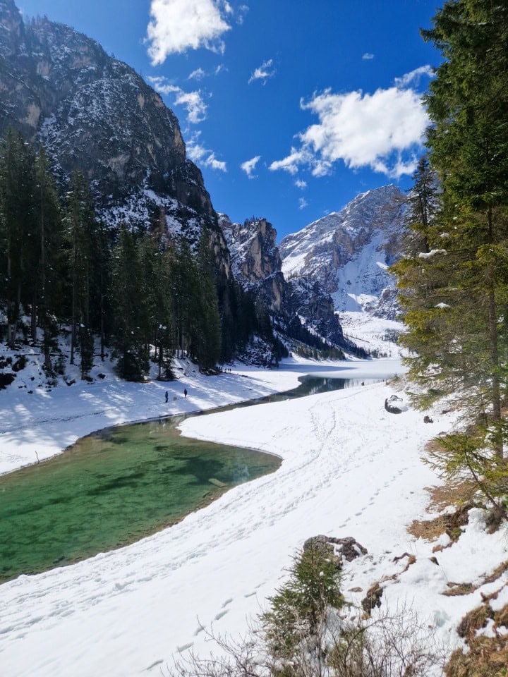 turquoise green waters or river braies, with snow and snowy mountains around it; dolomites italy