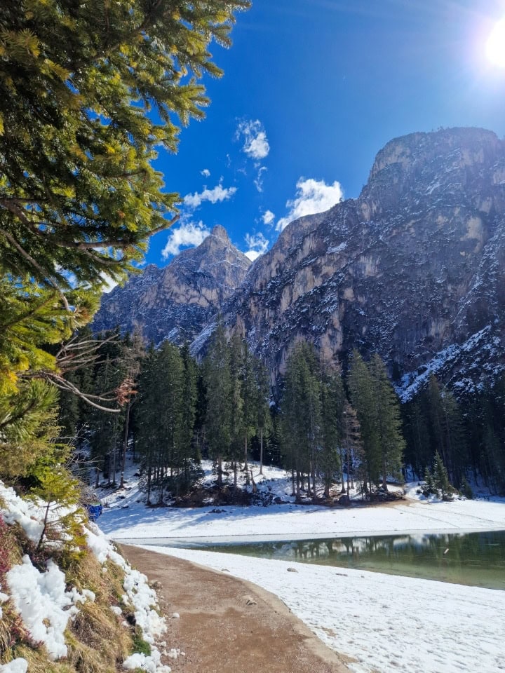 lago braies with turquoise green waters, mountains, snow, blue sky, and sun. april in dolomites italy