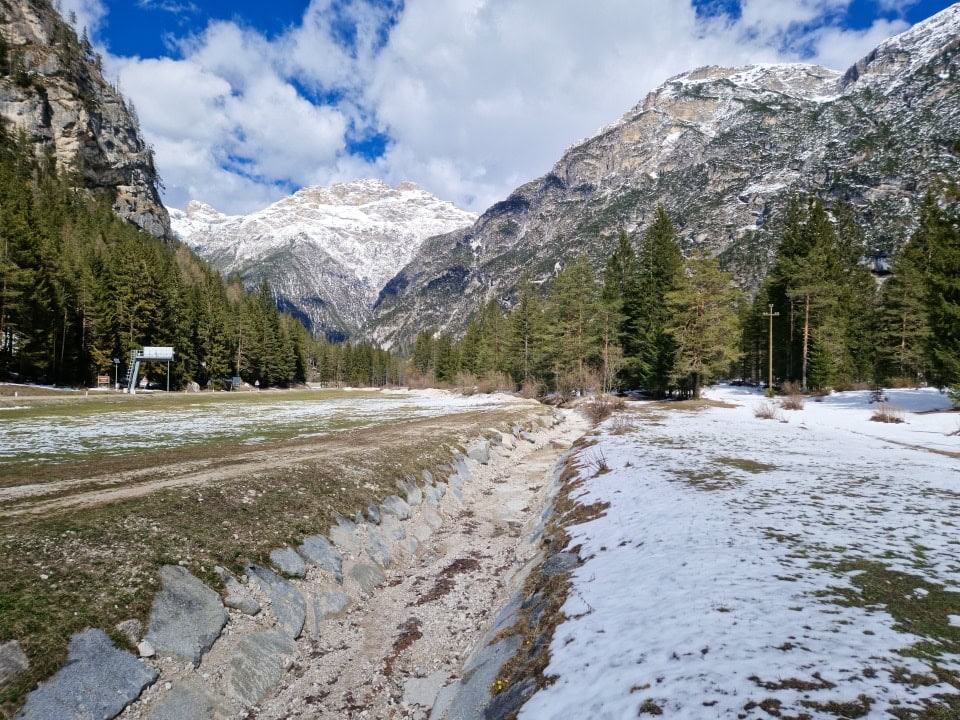 a dry river bed in april in dolomites with snow and snowy mountains around it/ italy