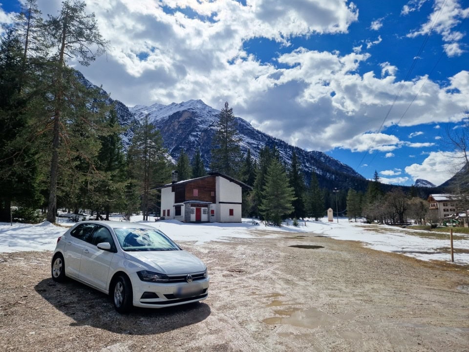 a car parked in a wet and snowy parking lot with mountains around it in dolomites italy