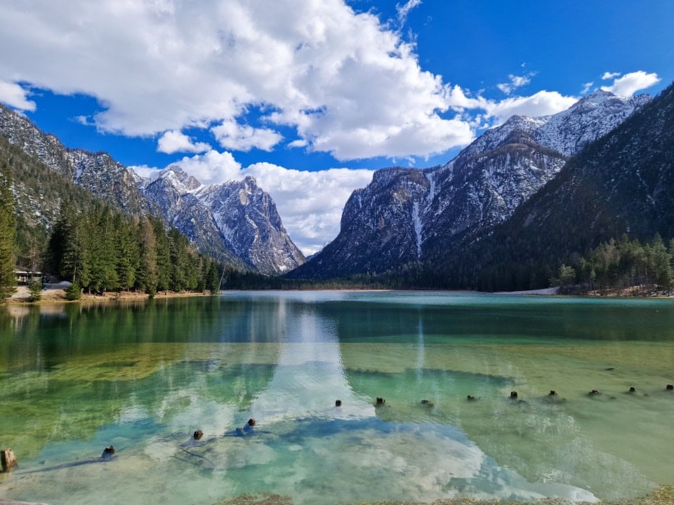 lago di dobbiaco with turquoise green waters and mountains behind it in dolomites italy