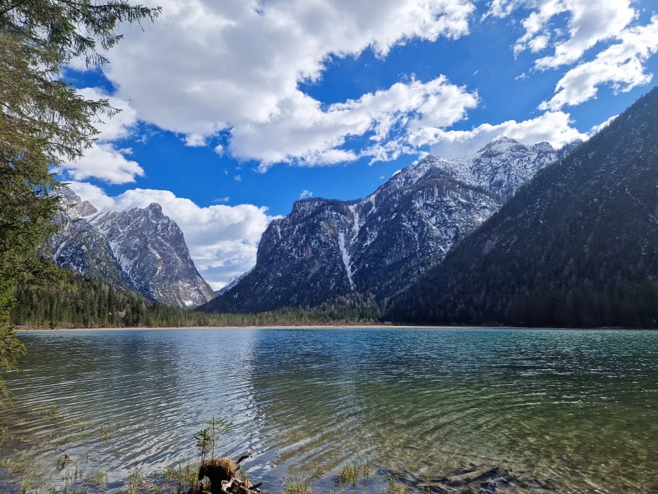 a side view of lago di dobbiaco with mountains behind it dolomites italyh