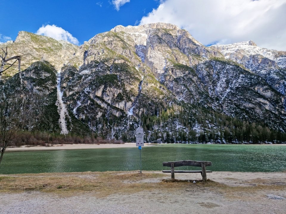 a bench by a turquoise green lago di landro with mountains in the background in dolomites italy