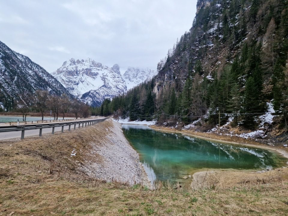 a turquoise pond next to lake landro with snowy mountains in the background in dolomites italy