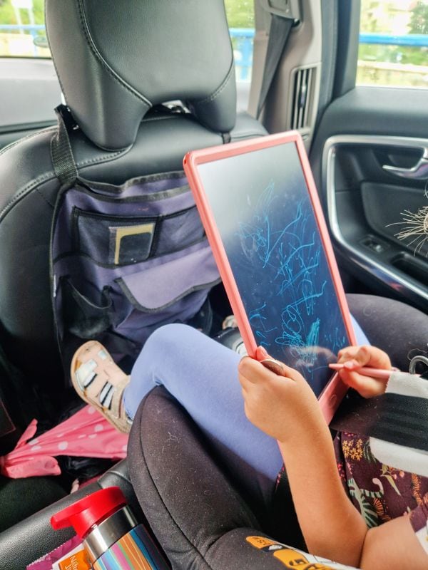 a kid drawing on a magnetic blackboard with a car seat organizer in the background